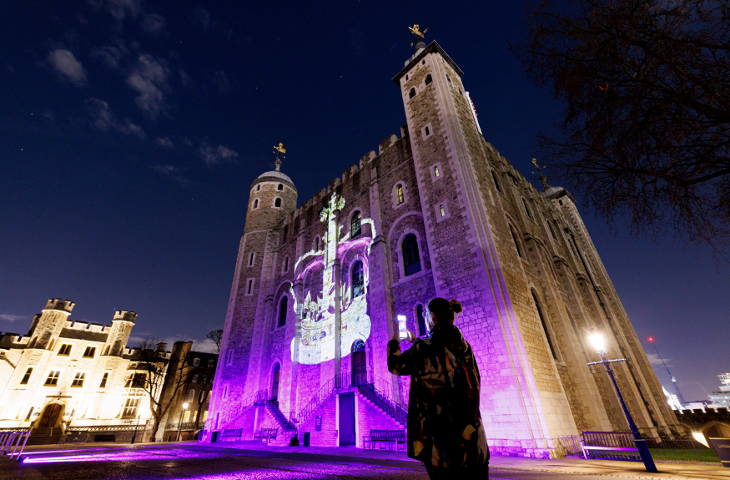 A woman takes a photo of a crown projection on the side of the White Tower