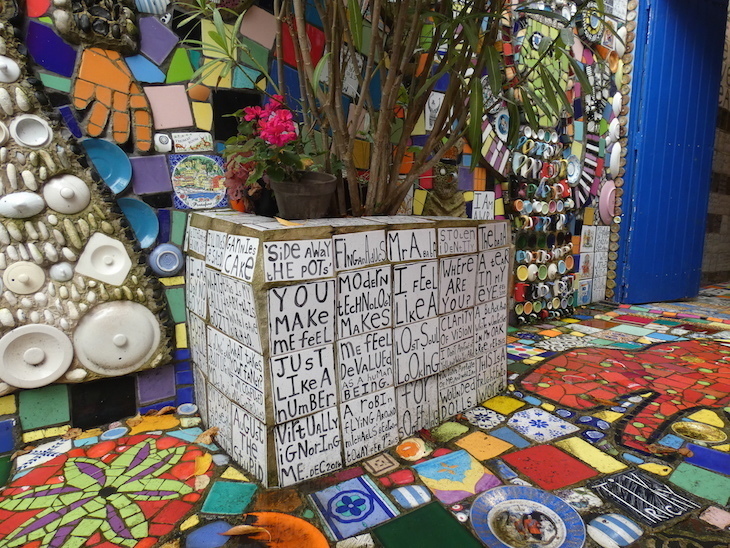 A corner of a garden completely covered in colourful tiles and mosaics