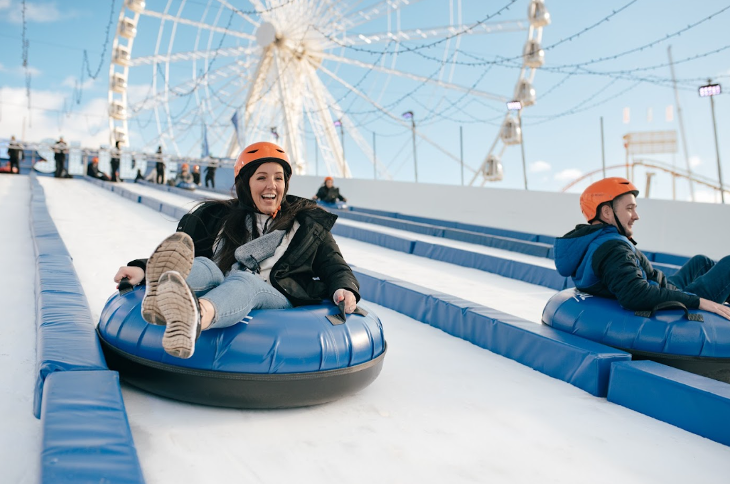 Two adults on inflatables riding down an ice slide