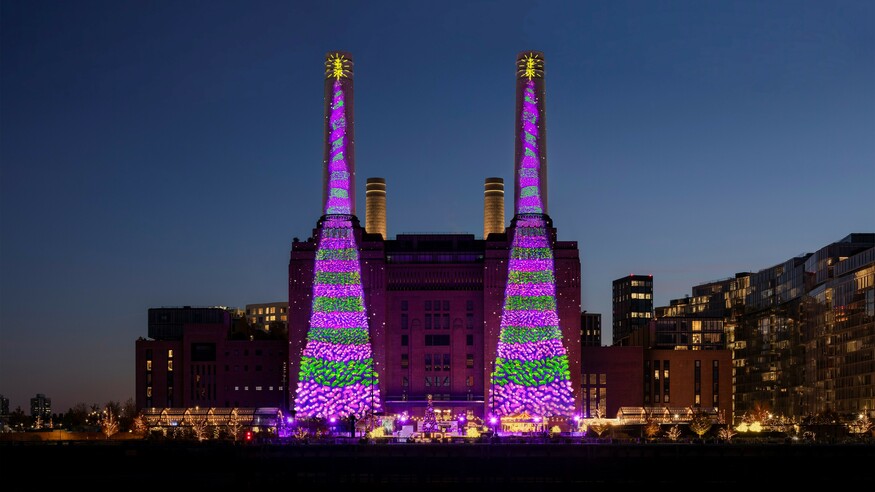Two purple and green Christmas trees projected on the side of Battersea Power Station
