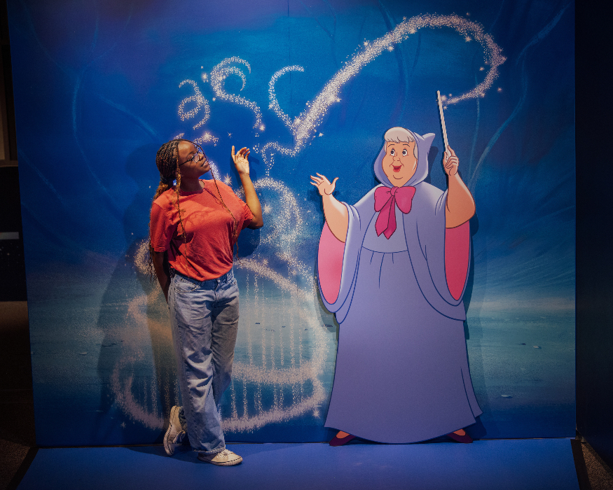 A woman posing in front of a screen depicting the fairy godmother from Cinderella
