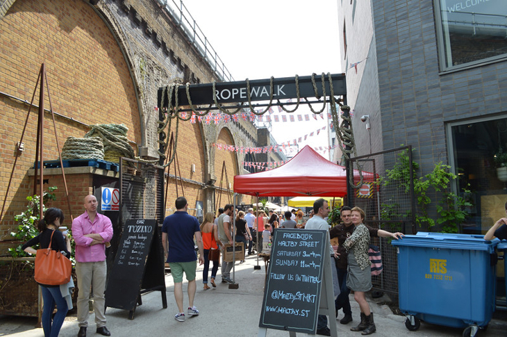 People walking into Maltby Street Market, in an alleway alongside the railway arches