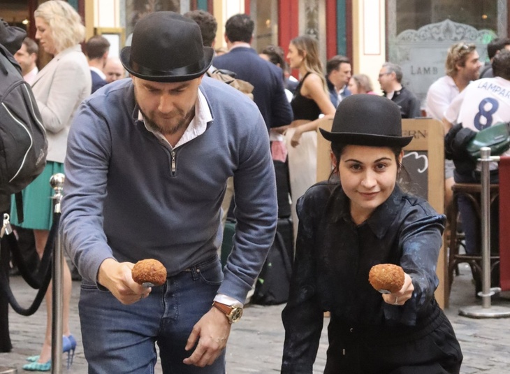 Two people in bowler hats ready to race with scotch eggs on spoons