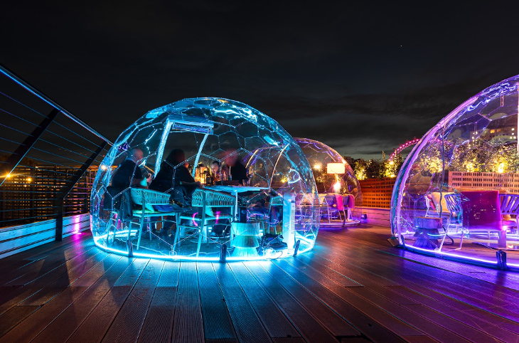 Igloo restaurants in London: A rooftop bar with neon-lit see-through igloo pods, and the London Eye illuminated in the distance