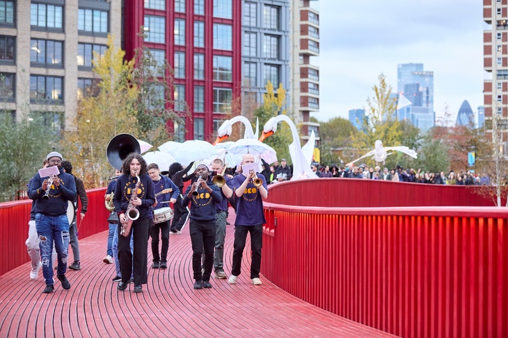 Musicians parading over the bridge with huge swan puppets behind them