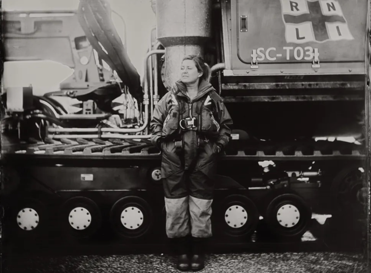 Black and white photo of a woman standing in front of an RNLI lifeboat