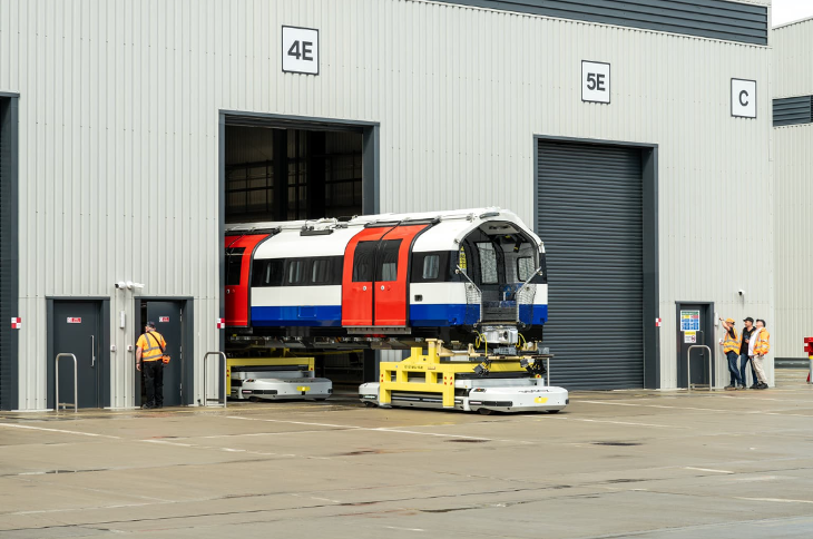 Photo of a new Piccadilly line train emerging from the side of a factory building