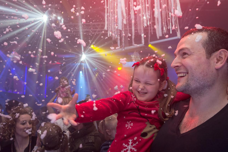 A man holding a young girl as fake snow falls on them