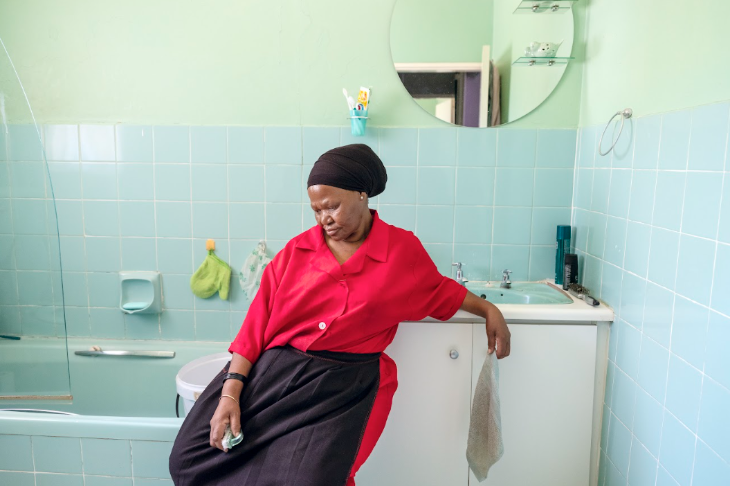 A photograph of a woman in a bathroom with a cleaning cloth in her hand