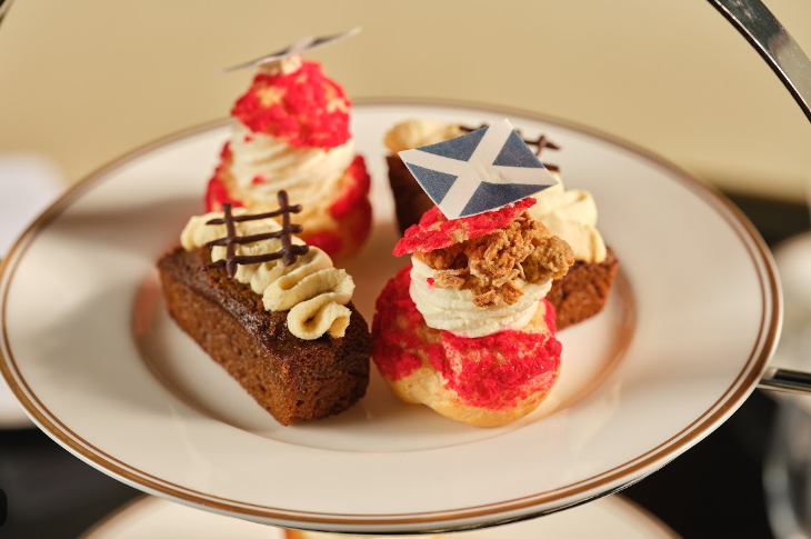 A plate holding four cakes and pastries, including one topped with the Scottish flag