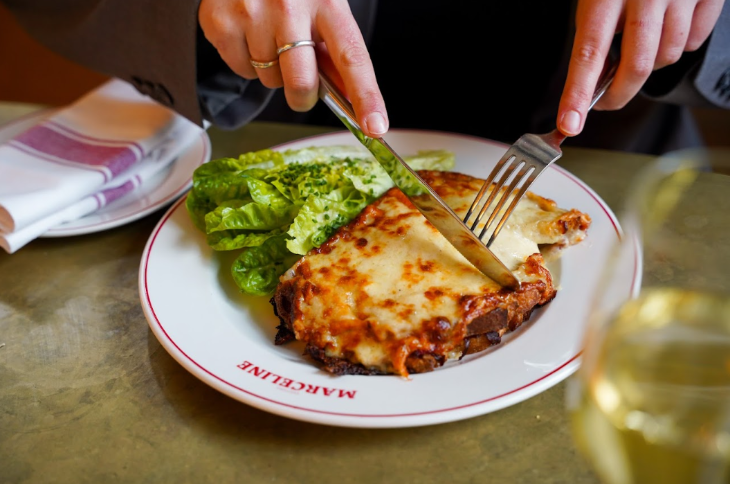 A close-up of a knife and fork being used to cut a croque monsieur
