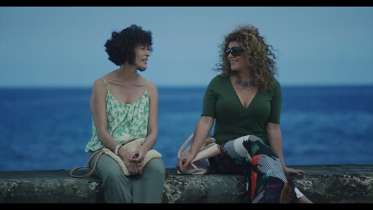 Two people sitting on a wall with the sea behind them