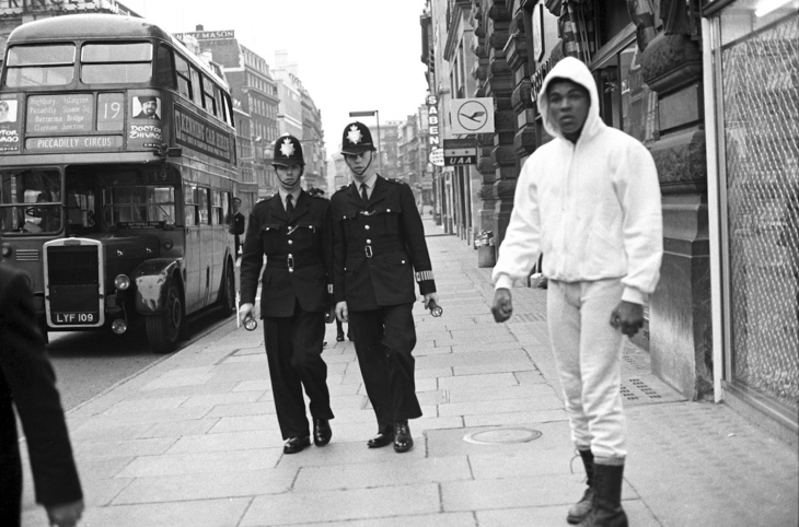 Muhammed Ali, with two bobbies and a London bus behind him