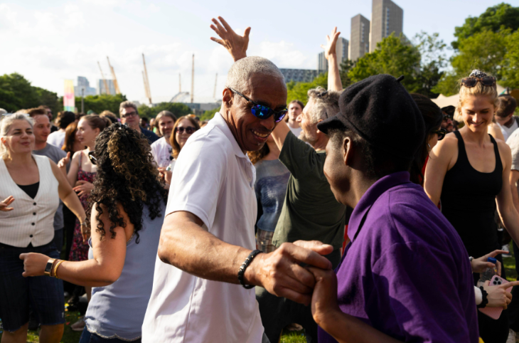 People dancing in the open-air, with the masts of the O2 dome visible in the distance