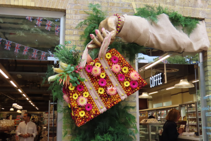 A large 3D arm holding a bag made from flowers, stuck onto the side of a building