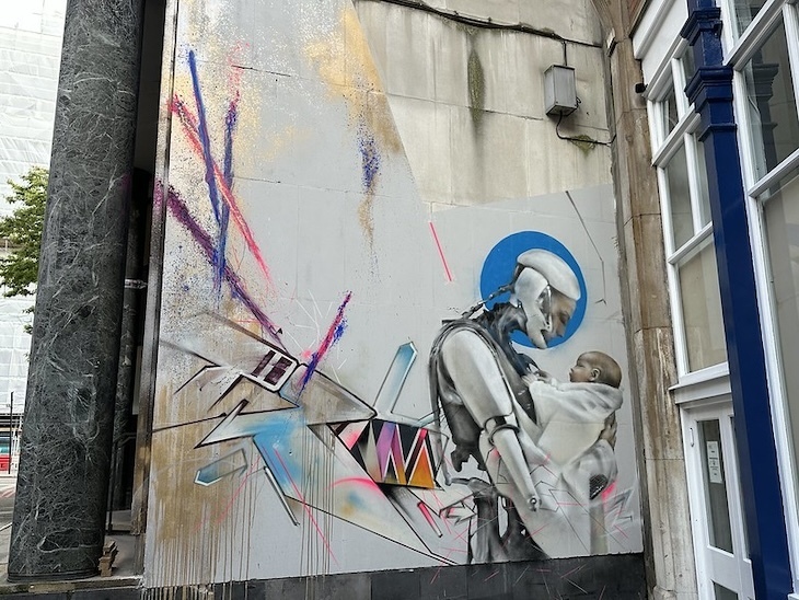 A street art cyborg holding a child