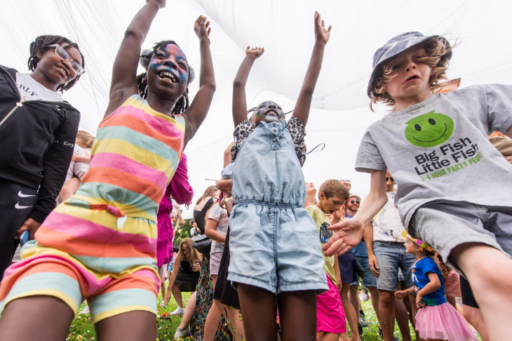 Children, some with faces painted, dancing beneath a giant parachute