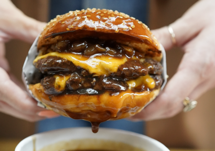 A pair of hands holding a burger, dripping with gravy