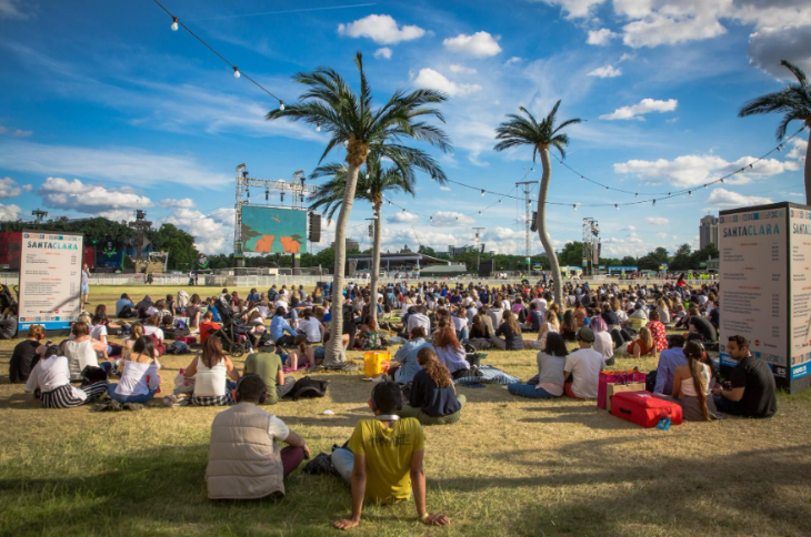 Outdoor cinema London 2025: People sitting on the grass among palm trees and food stalls, watching a large screen