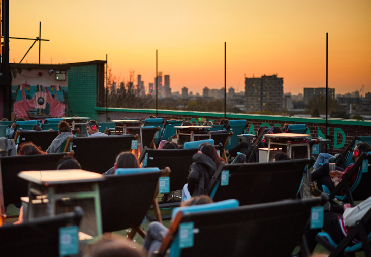 Deckchairs arranged on a rooftop at sunset, with the local skyline in the background