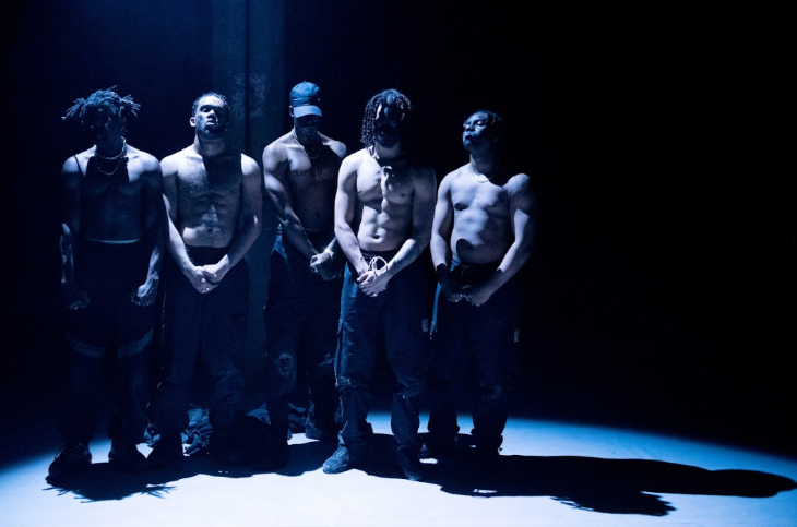 Five dancers lined up in the spotlight, with their hands held in front of them