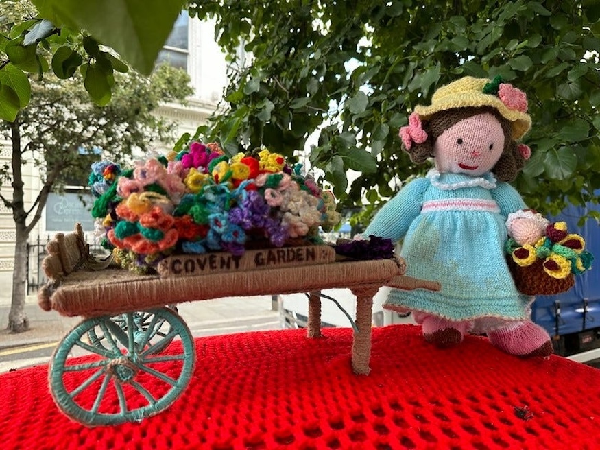 A post box crocheted scene of a flower girl with barrow