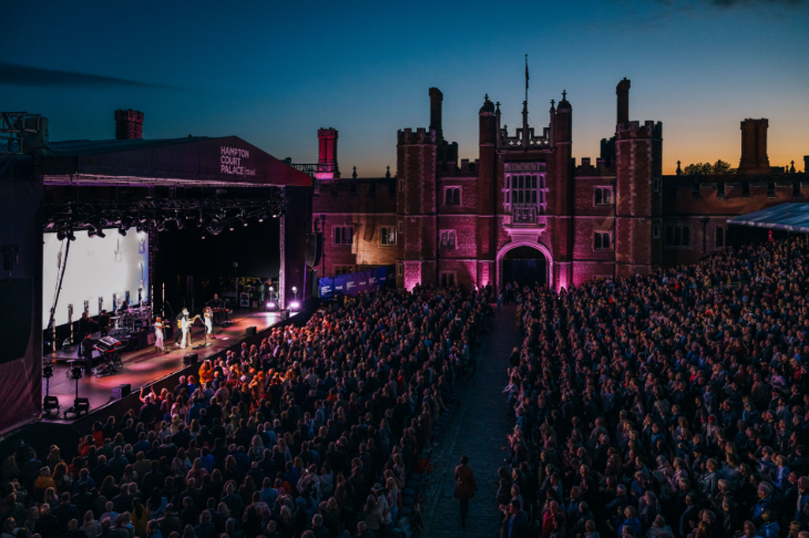 People sitting in stands watching a concert outside Hampton Court Palace