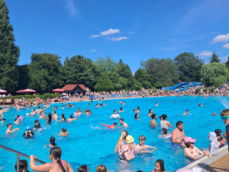 Lots of people in an outdoor swimming pool, with slides on the opposite side of the pool