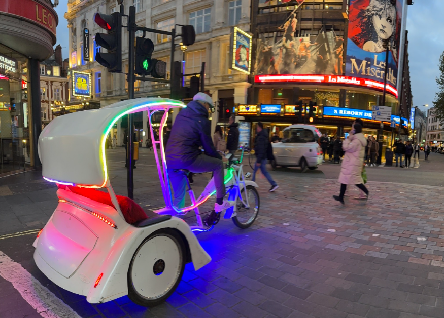 An illuminated pedicab passing a London theatre