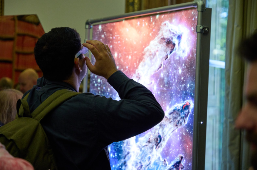 A man wearing special glasses looking at an illuminated picture of space