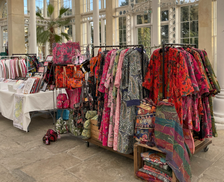 Racks of colourful dresses alongside a stall inside a conservatory