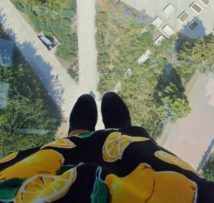 A pair of feet on a glass floor, with a park far below