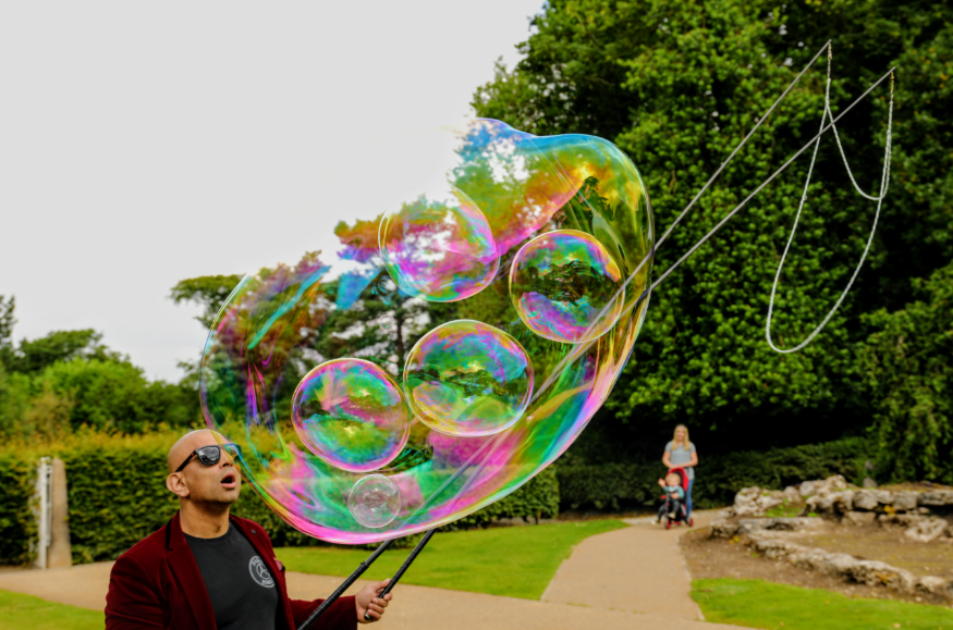 Summer holidays 2025 in London: a man in a park or garden, using wands and string to create giant bubbles