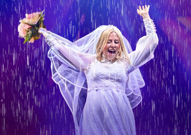 A woman on stage in a wedding dress in the rain