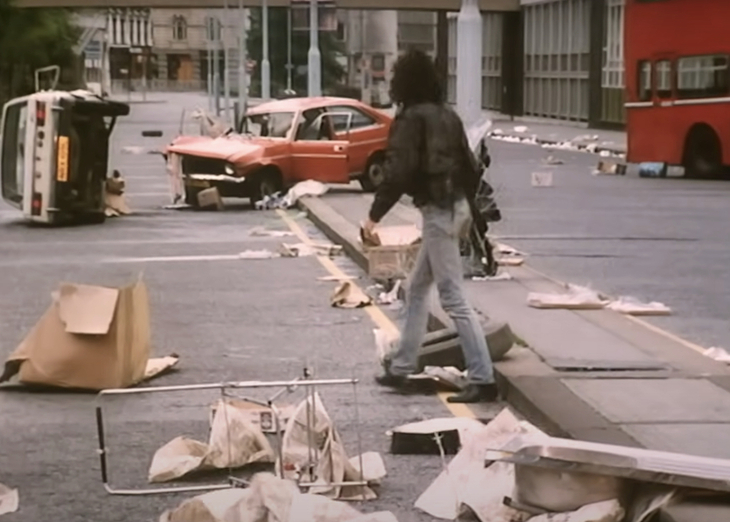 A bedraggled man walking through a bedraggled street