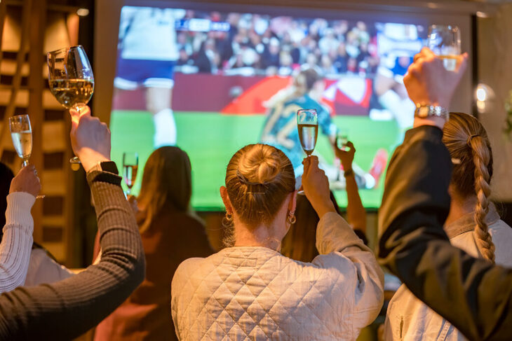People raising wine glasses in front of a big screen