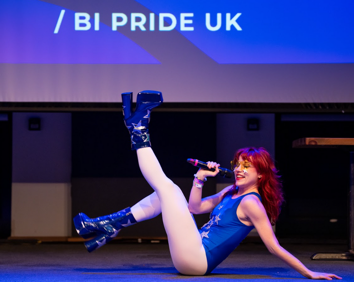 Things to do in London August 2025: a performer sitting down on stage kicking their legs in the air, with a microphone in one hand