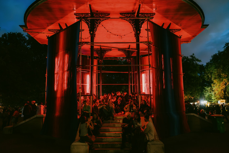 August bank holiday weekend 2025 London: people sitting in an illuminated bandstand in a park at dusk