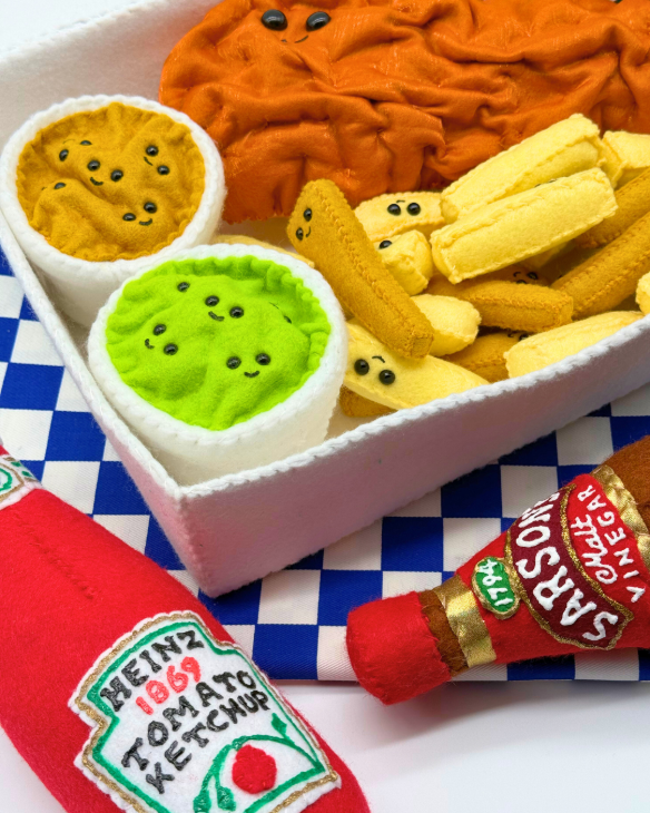 A chip shop box containing chips and a pot of mushy peas, alongside bottles of ketchup and vinegar, all of which is made from felt