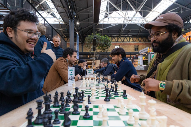 People facing each other over a row of chess boards
