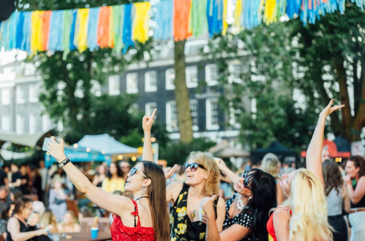 People posing for a photo with their arms in the air, beneath colourful bunting