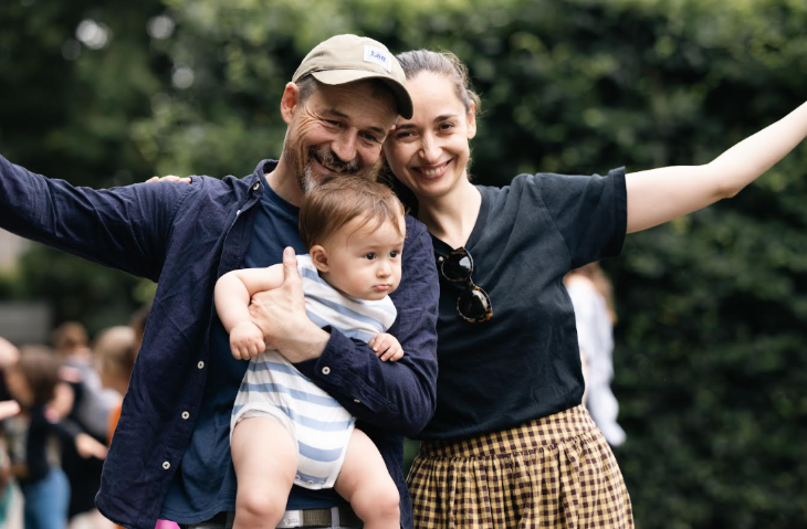 A man and a woman holding a baby and dancing together in a park
