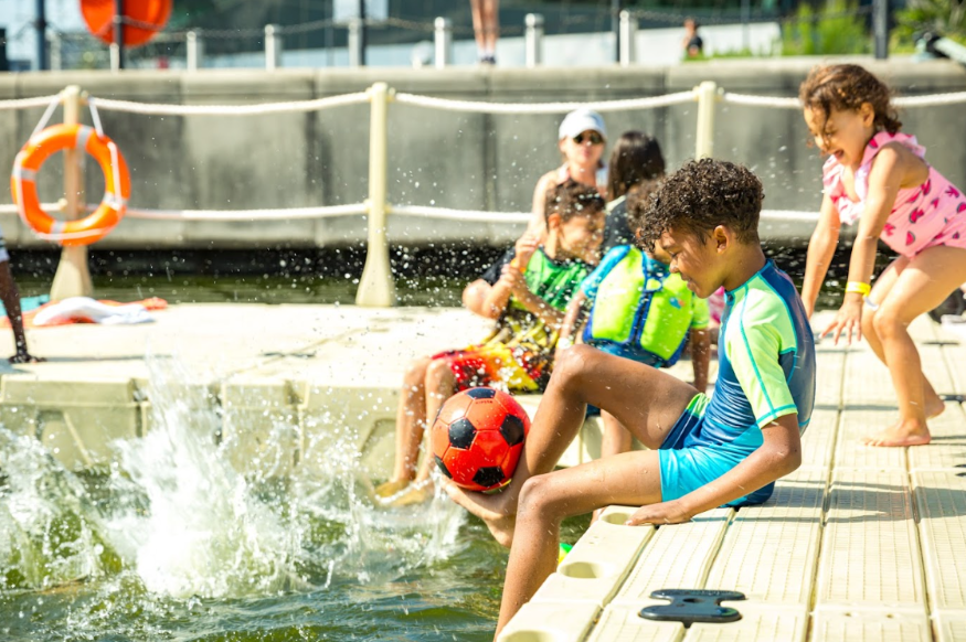 A boy sitting on the edge of a lido, splashing his legs in the water