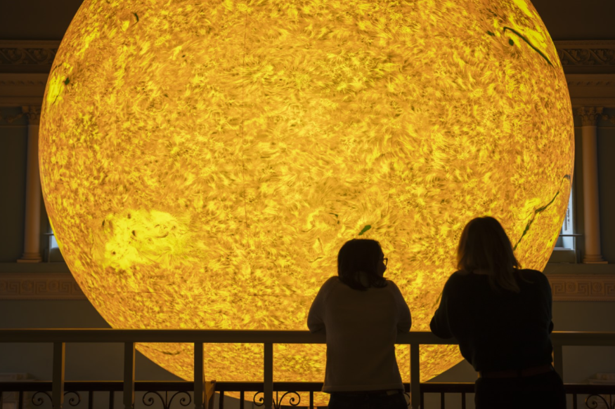 Two people silhouetted in front of a glowing replica of the sun