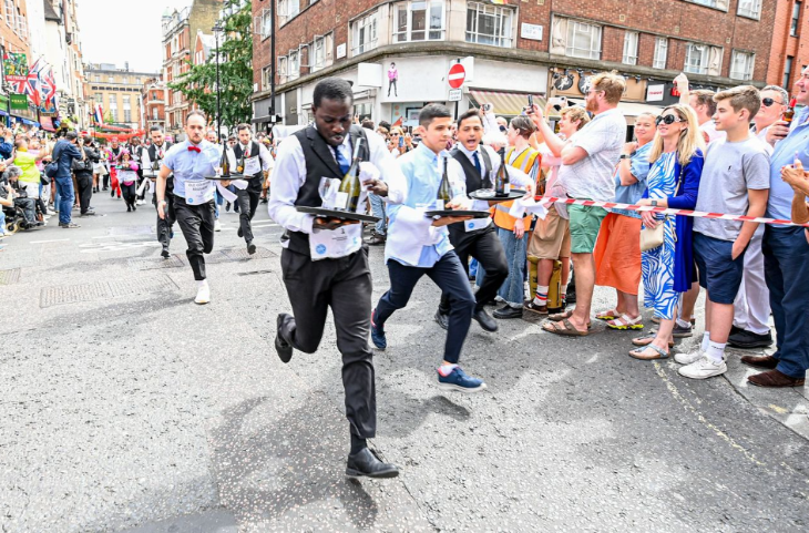 Crowds cheering on waiters who are racing while holding trays with bottles
