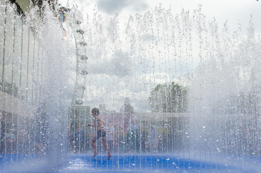 Play fountains in London: a boy running through fountain jets in front of the London Eye