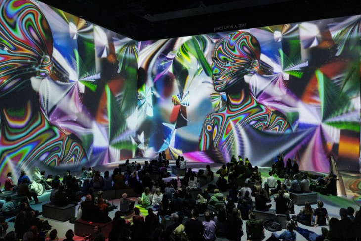 Things to do in London August 2025: people sitting on the floor in a large room with projections on the walls and ceiling around them