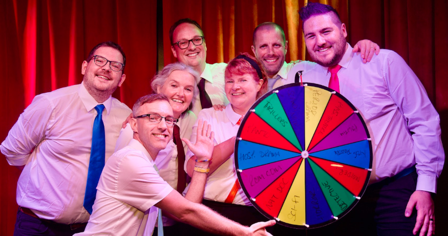 Things to do in London this weekend: seven people posing for a photo with a gameshow-style spinning wheel