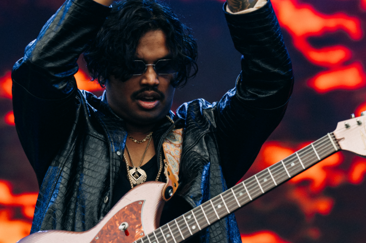 Things to do today in London: a musician on stage with a guitar strapped on him, clapping his hands in the air