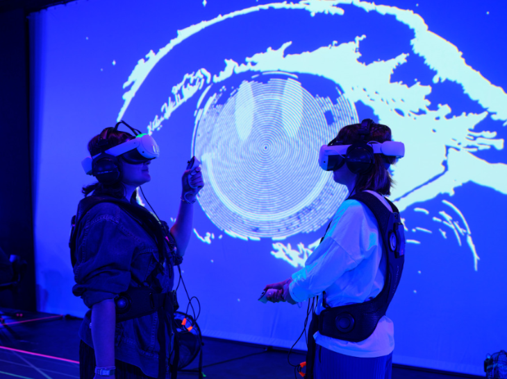 Things to do today in London: two people wearing VR headsets in front of a blue screen depicting an eye